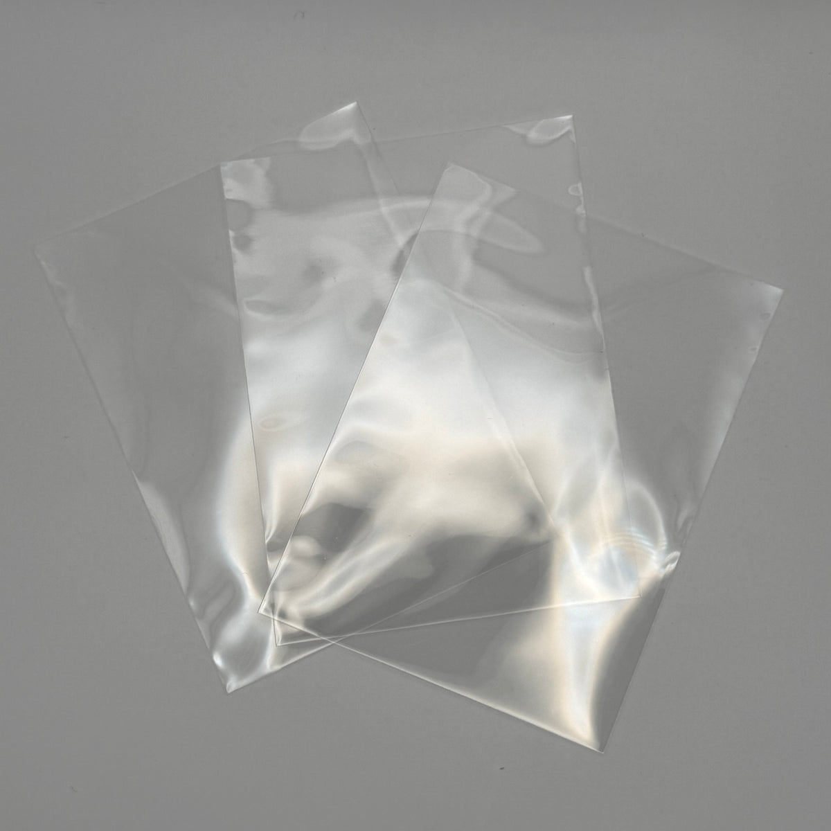 Three clear plastic bags of different sizes arranged in a fan shape on a neutral gray background.