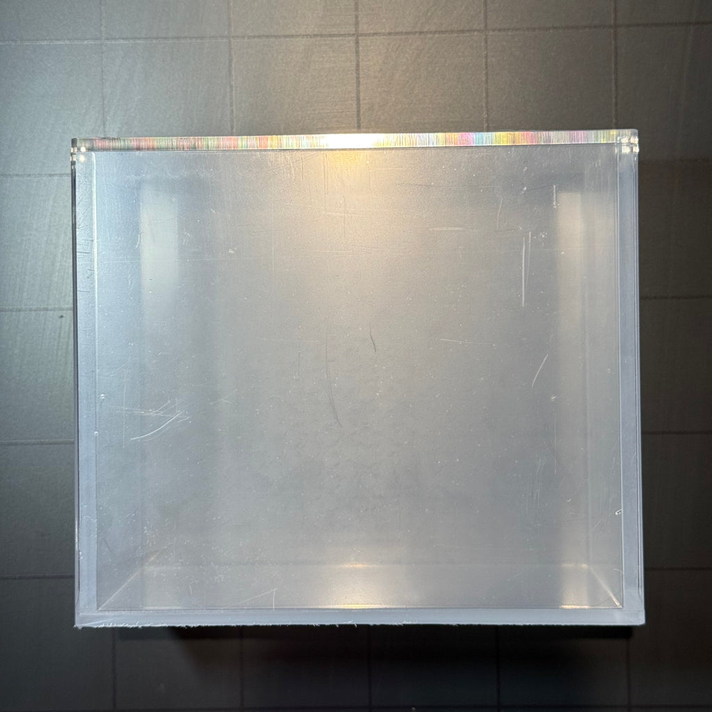 A clear acrylic or polycarbonate rectangular display box or shadow box with a hinged front, shown against a dark gray tiled background.