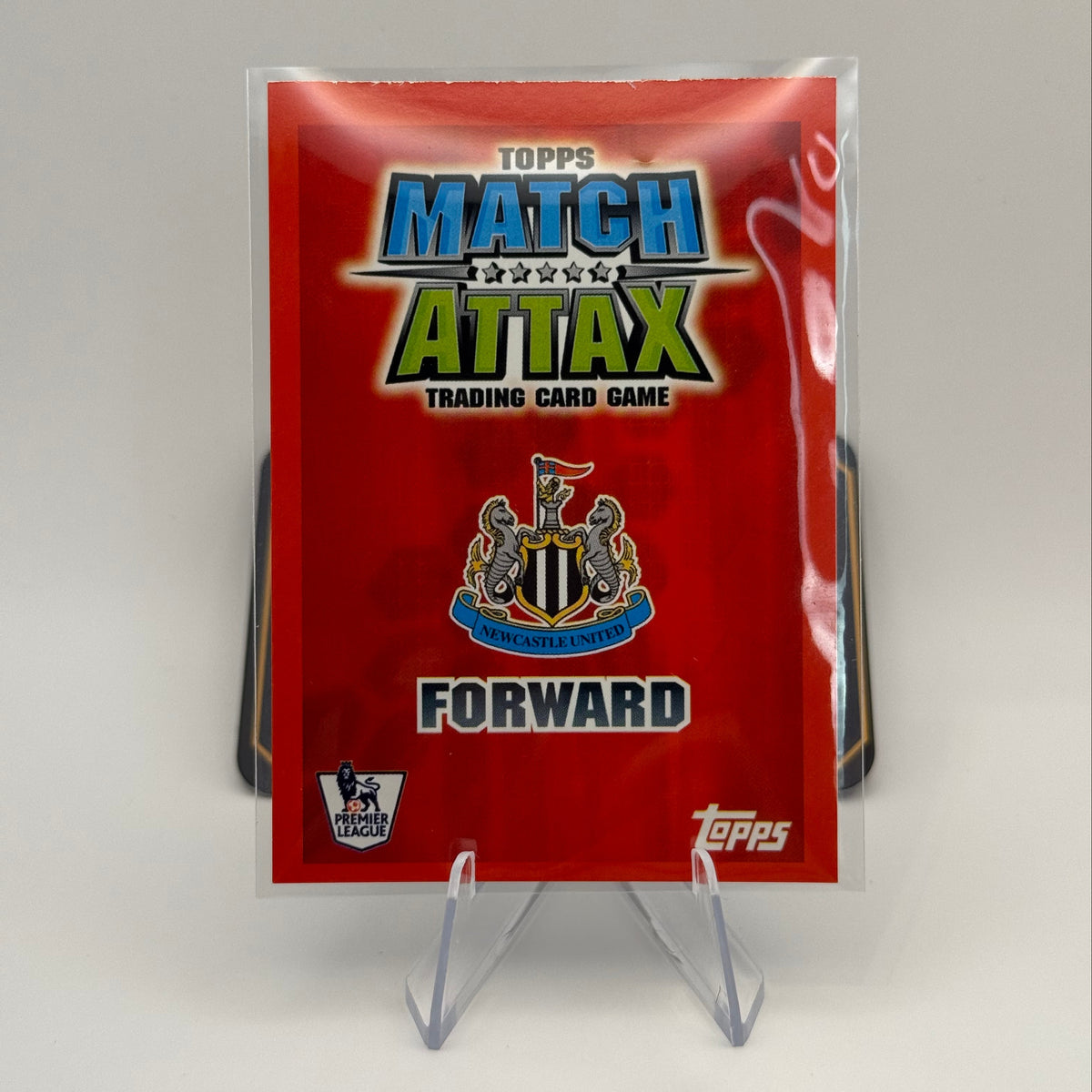 A sealed Topps Match Attax trading card game pack standing upright on a clear plastic display stand against a light gray background.